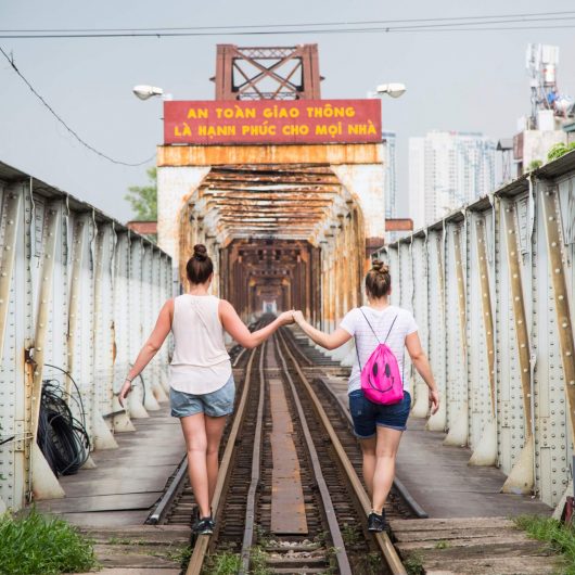 Turister går hånd i hånd på den berømte Long Bien bro i Hanoi