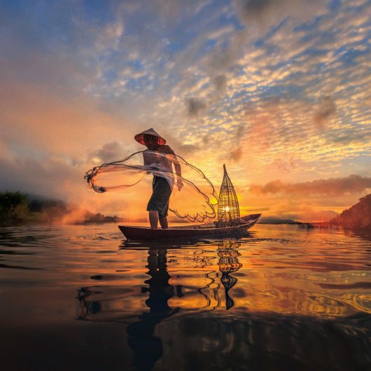 Fisker på Mekong-floden smider net med solopgangen i baggrunden